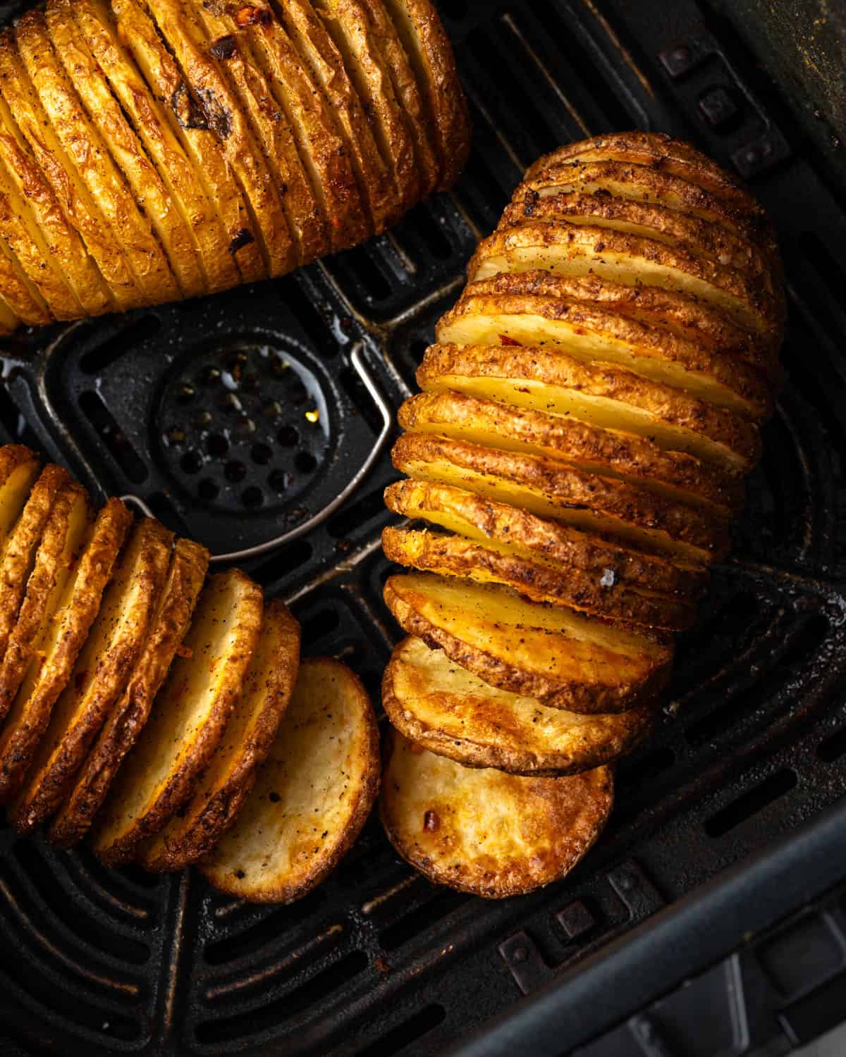Three cooked hasselback potatoes inside an air fryer basket. 