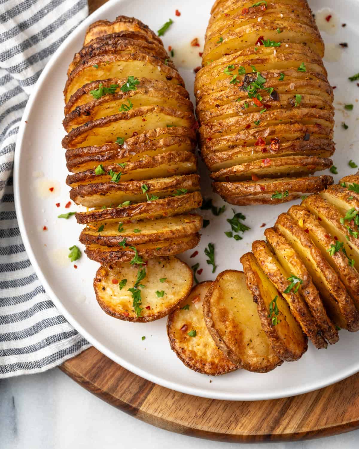 Three air fried hasselback potatoes topped with chopped parsley on a white plate.