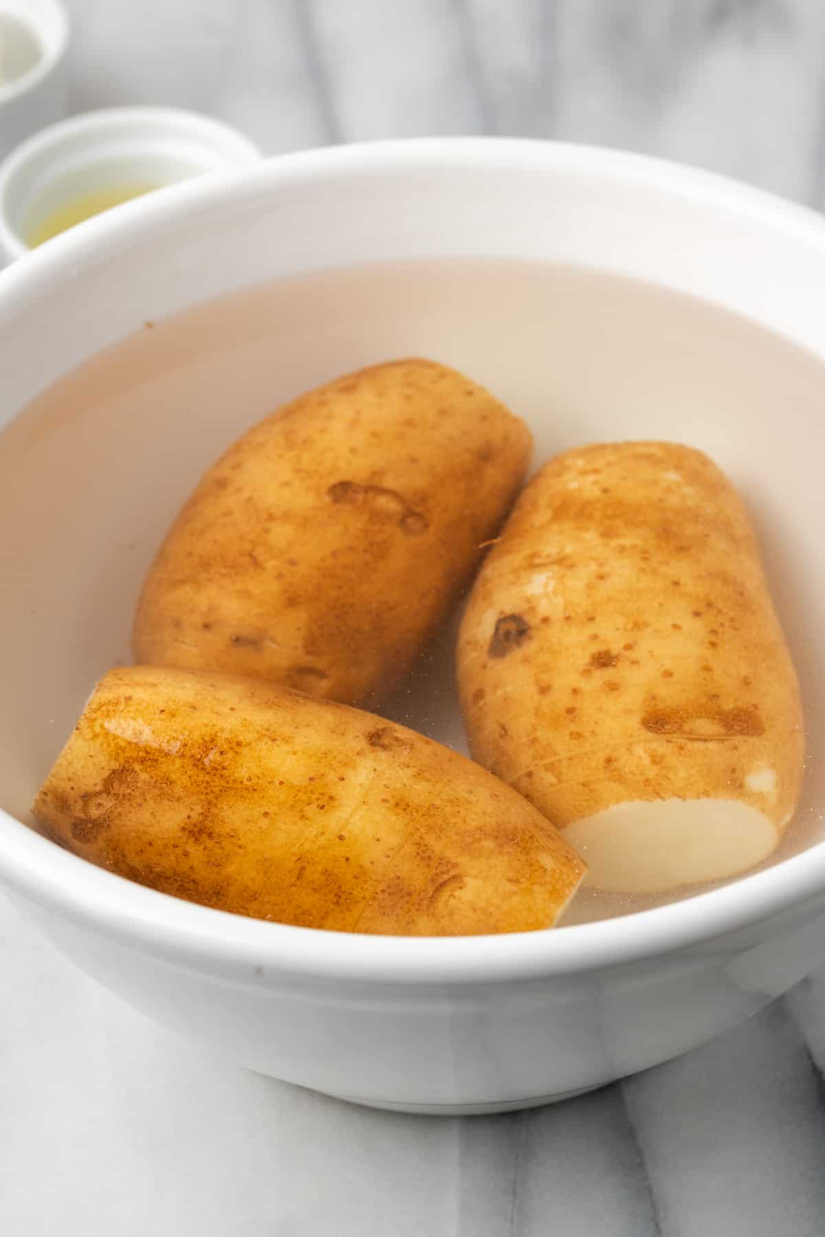 Three russet potatoes submerged in a large bowl full of water. 