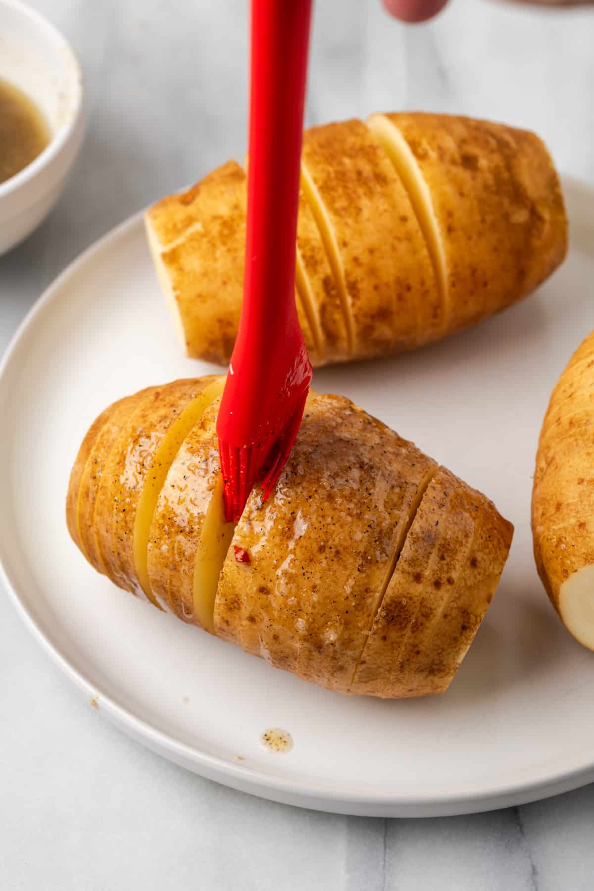 A silicone brush being used to brush the seasoned oil mixture in between slices of potato. 