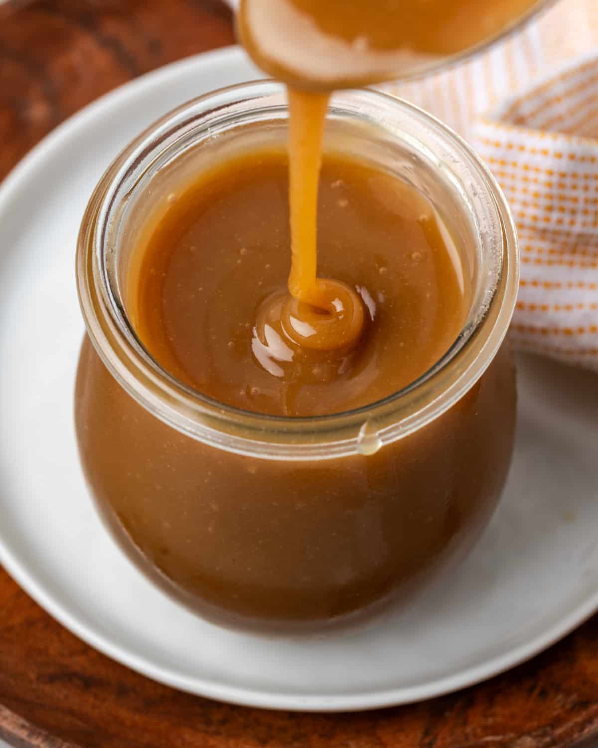 A small jar of apple cider caramel sitting on a white plate.