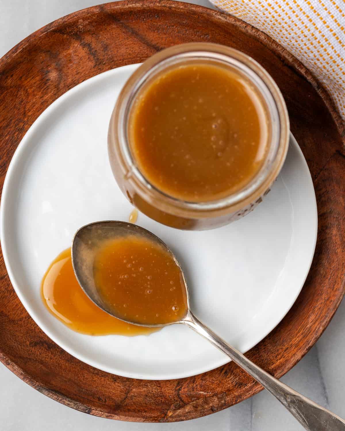 A spoon of caramel sauce sitting on a white plate next to a jar of caramel.