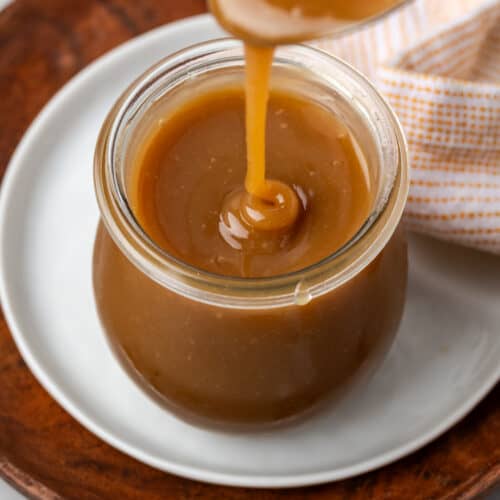 A jar of apple cider caramel sitting on a white plate.