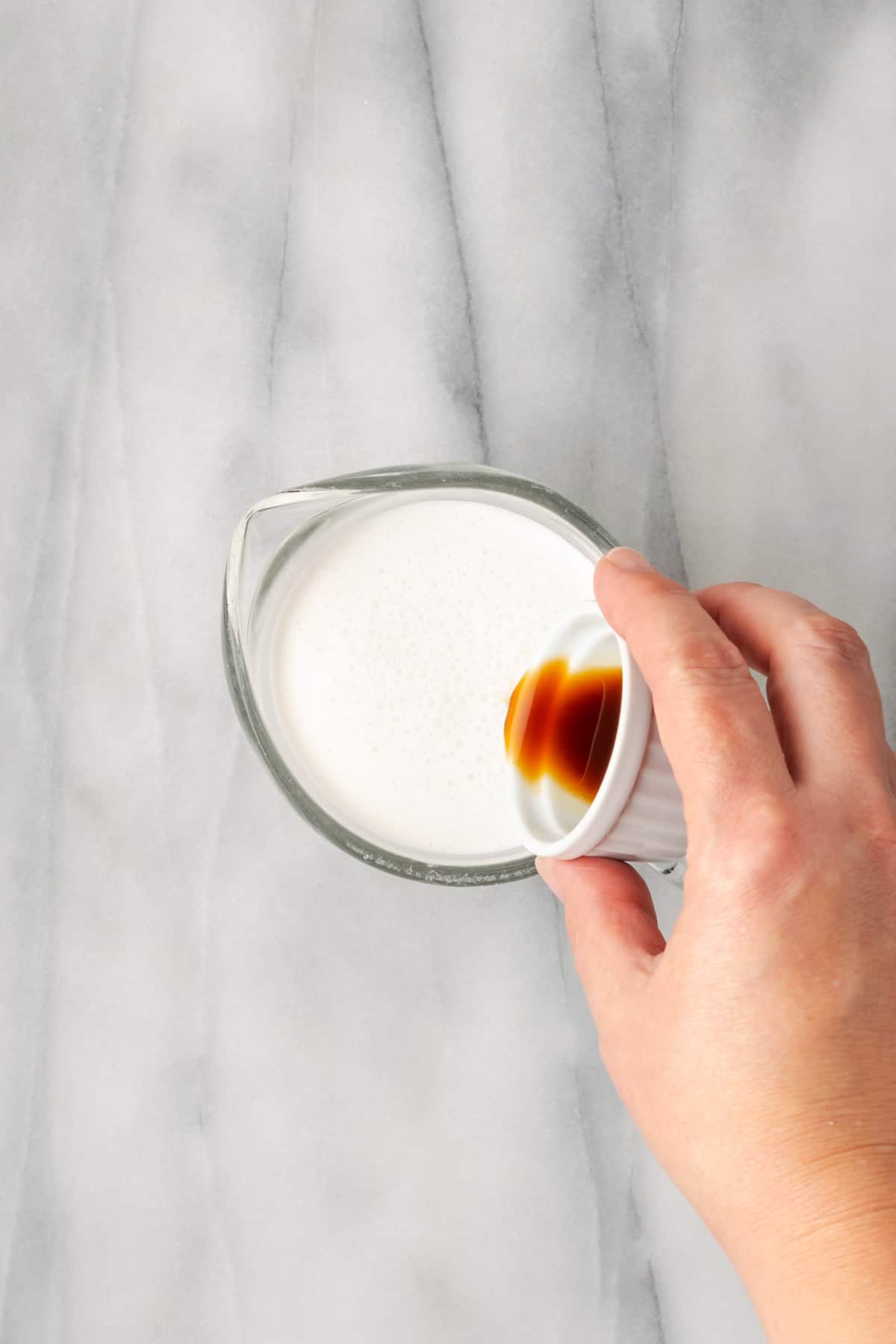 Vanilla being poured into a measuring cup filled with cream.