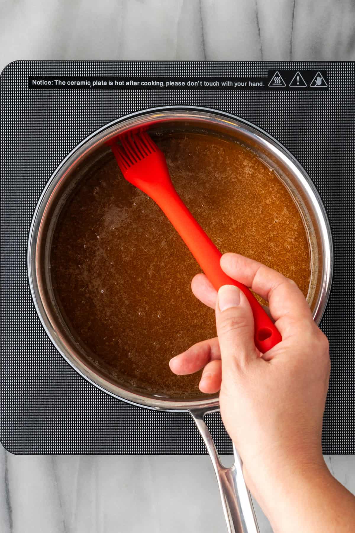 Using a pastry brush to wipe down the edges of the saucepan.