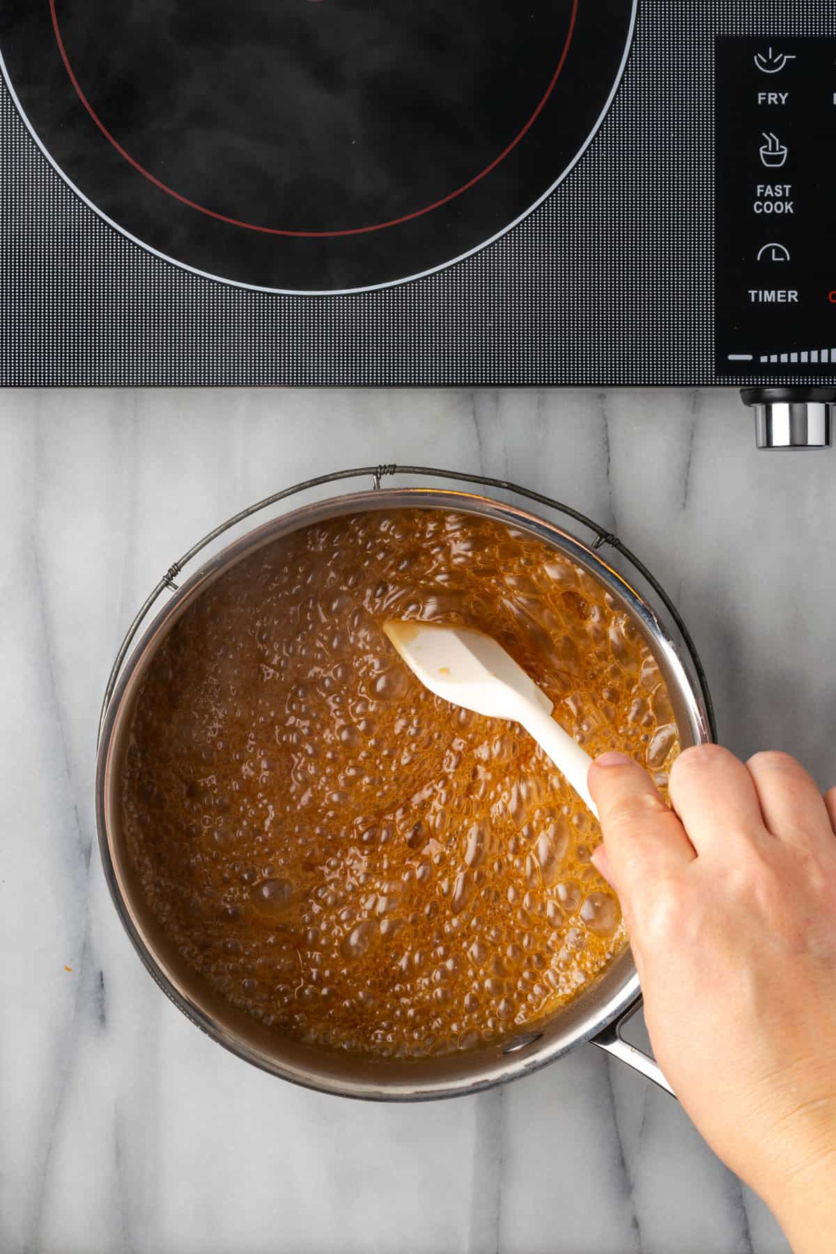 Stirring hot caramel sauce with a white spatula.