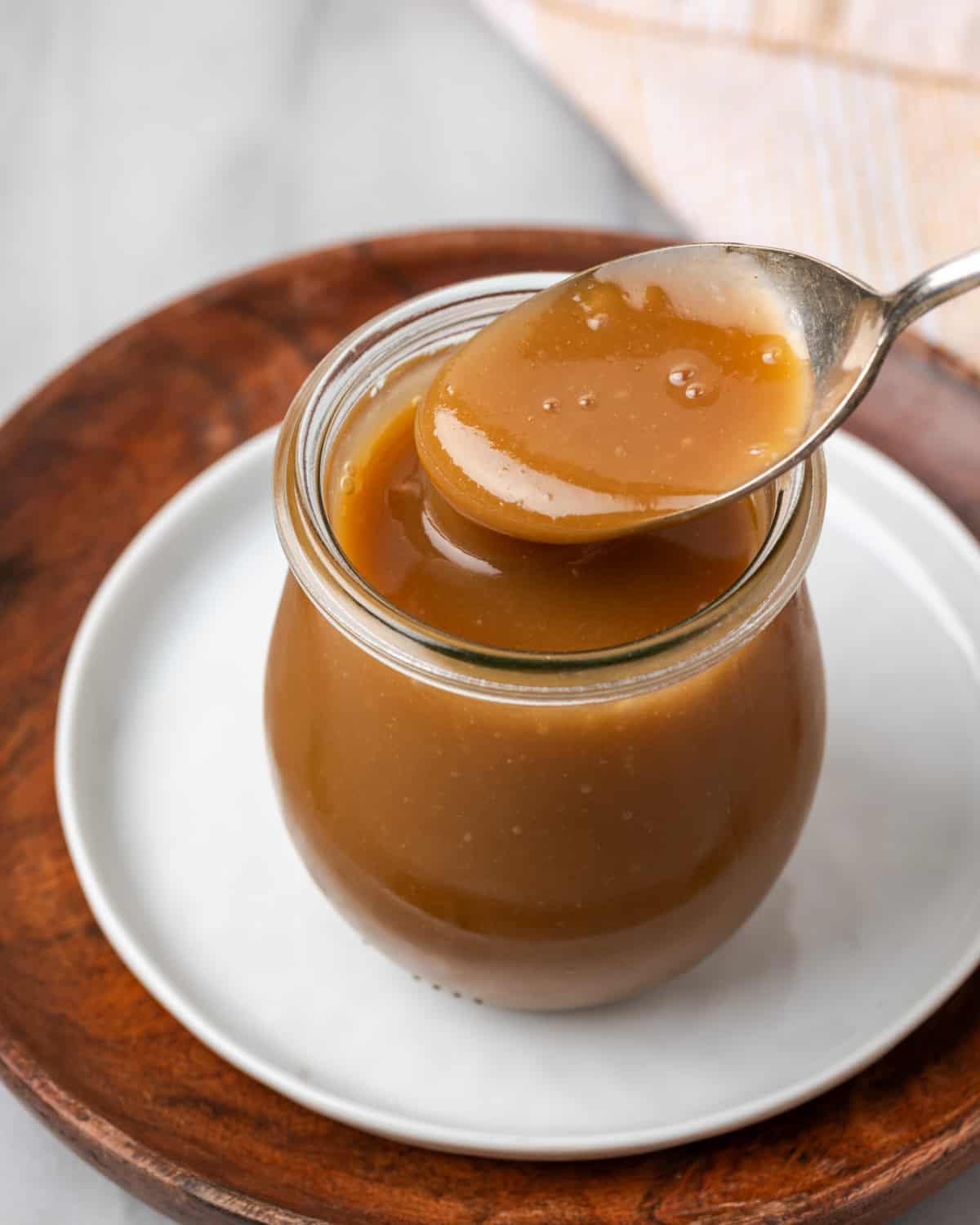 A spoon dipping into a jar of apple cider caramel sauce.