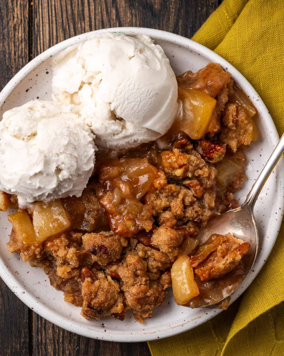 Gluten free apple crumble served on a white plate with two scoops of vanilla ice cream. 