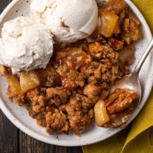 A serving of gluten free apple crumble with two scoops of vanilla ice cream on a white plate.