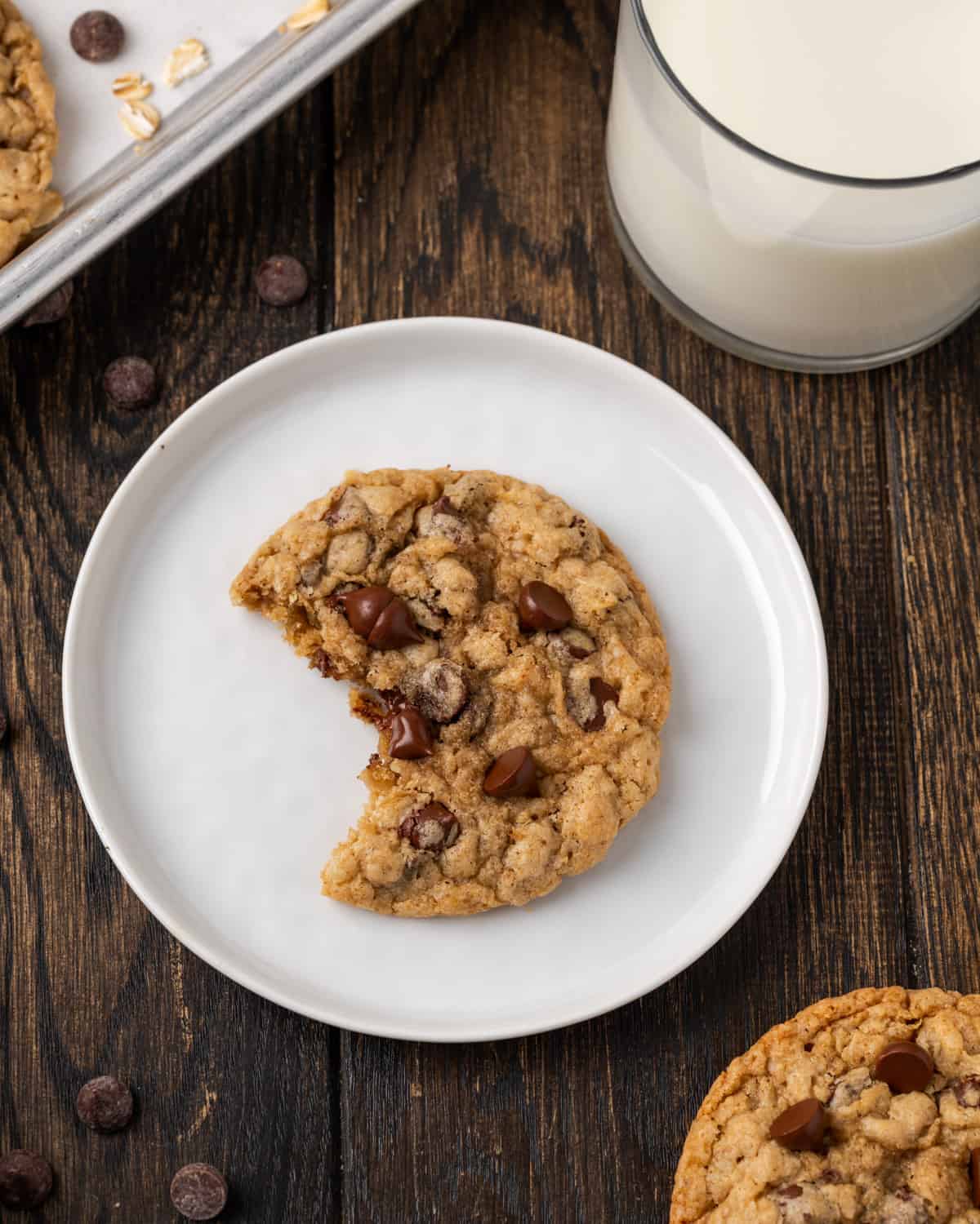 An oatmeal chocolate chip cookie with a bite taken out sitting on a plate.