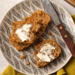 Two slices of gluten free zucchini bread spread with butter on a serving plate.