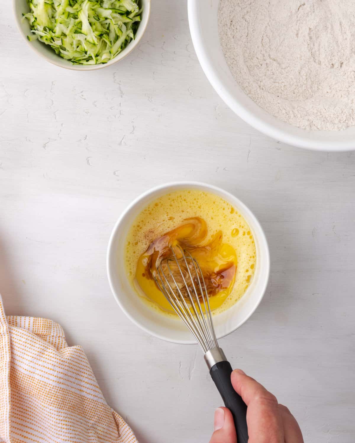 Oil, milk and vanilla being whisked into a bowl of beaten eggs. 