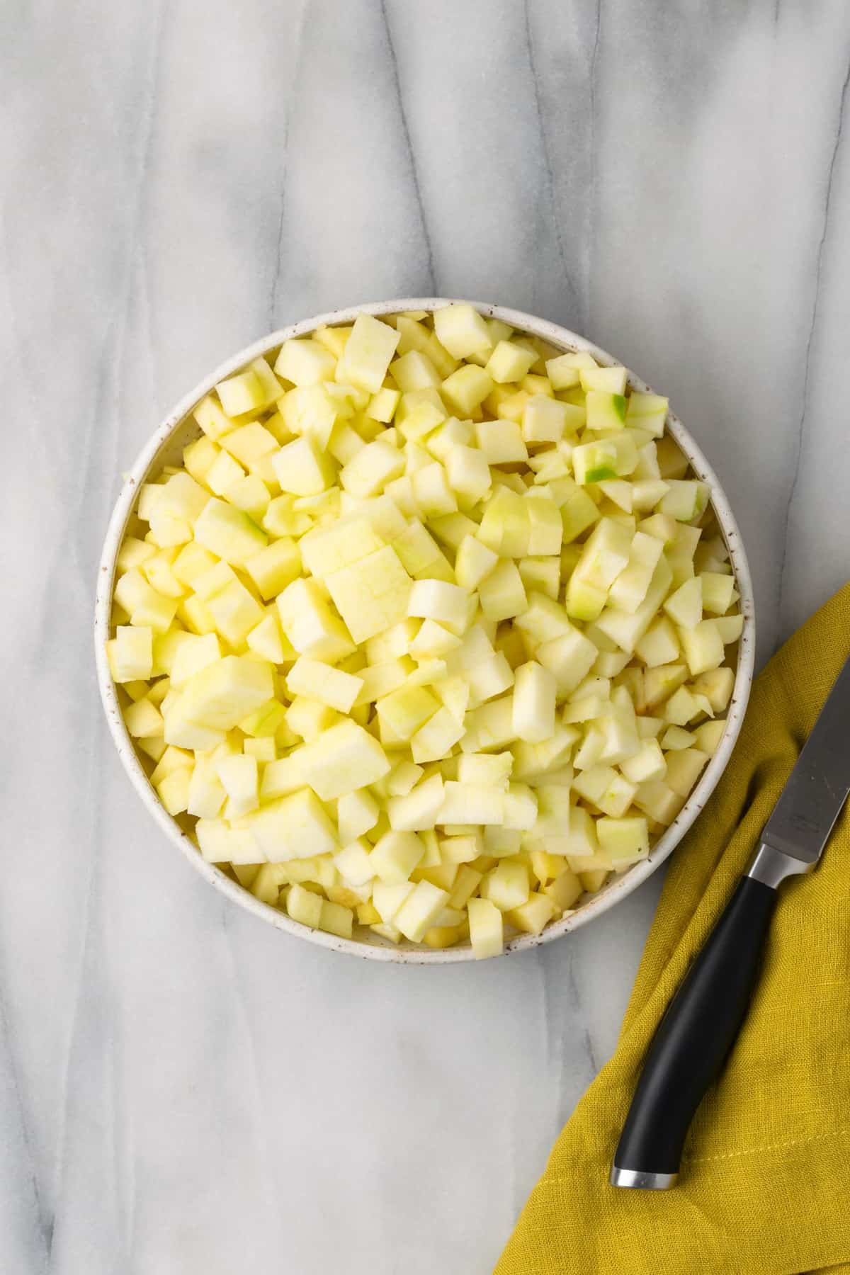 A white bowl filled with cut pieces of fresh apple.