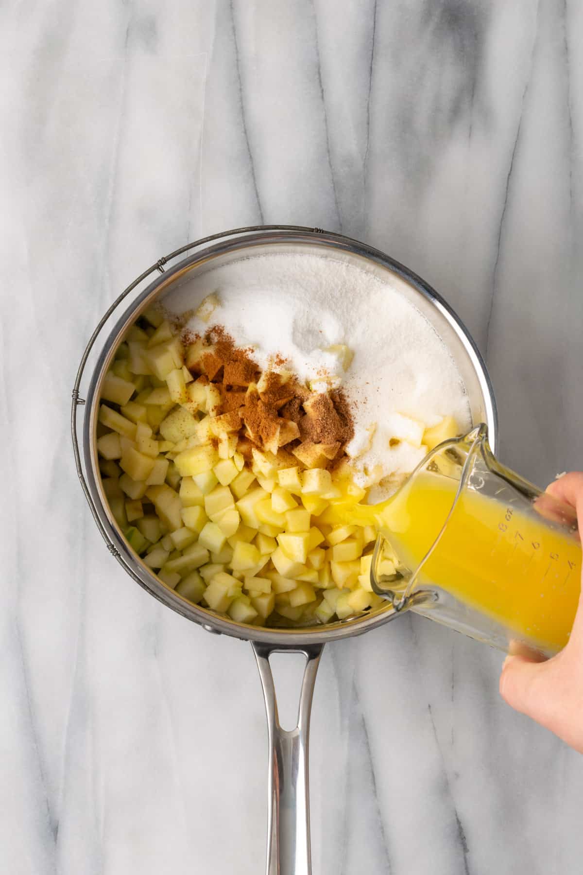 Sliced apples, sugar, orange juice, nutmeg and cinnamon added to the saucepan.