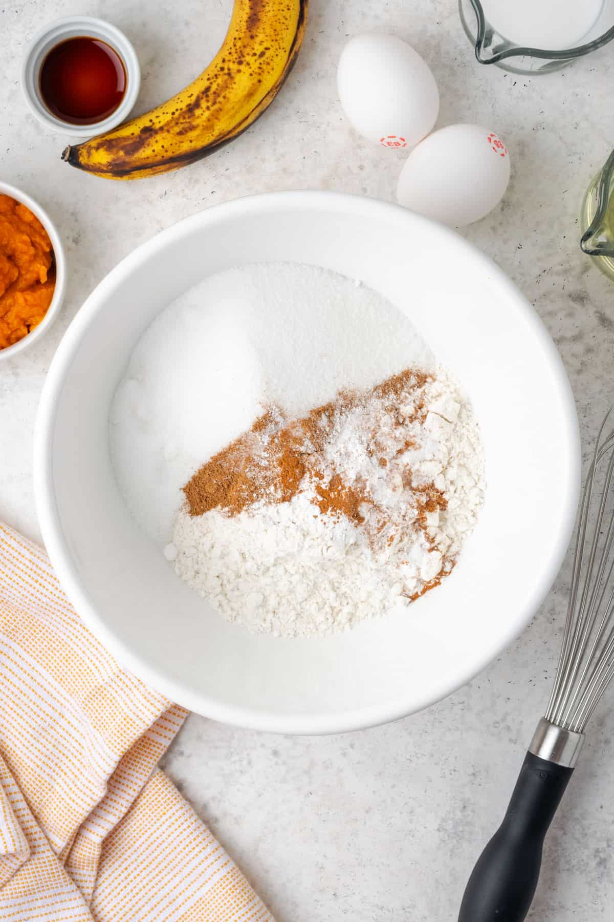 Gluten free flour, sugar, baking powder, baking soda, cinnamon, pumpkin spice and salt combined in a large white mixing bowl. 