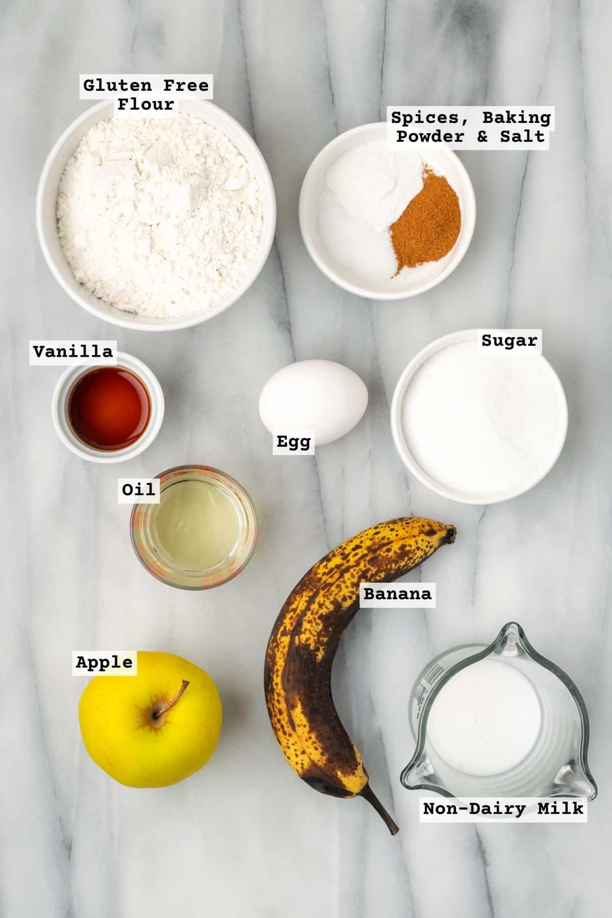 Ingredients for apple banana muffins on a white marble table.