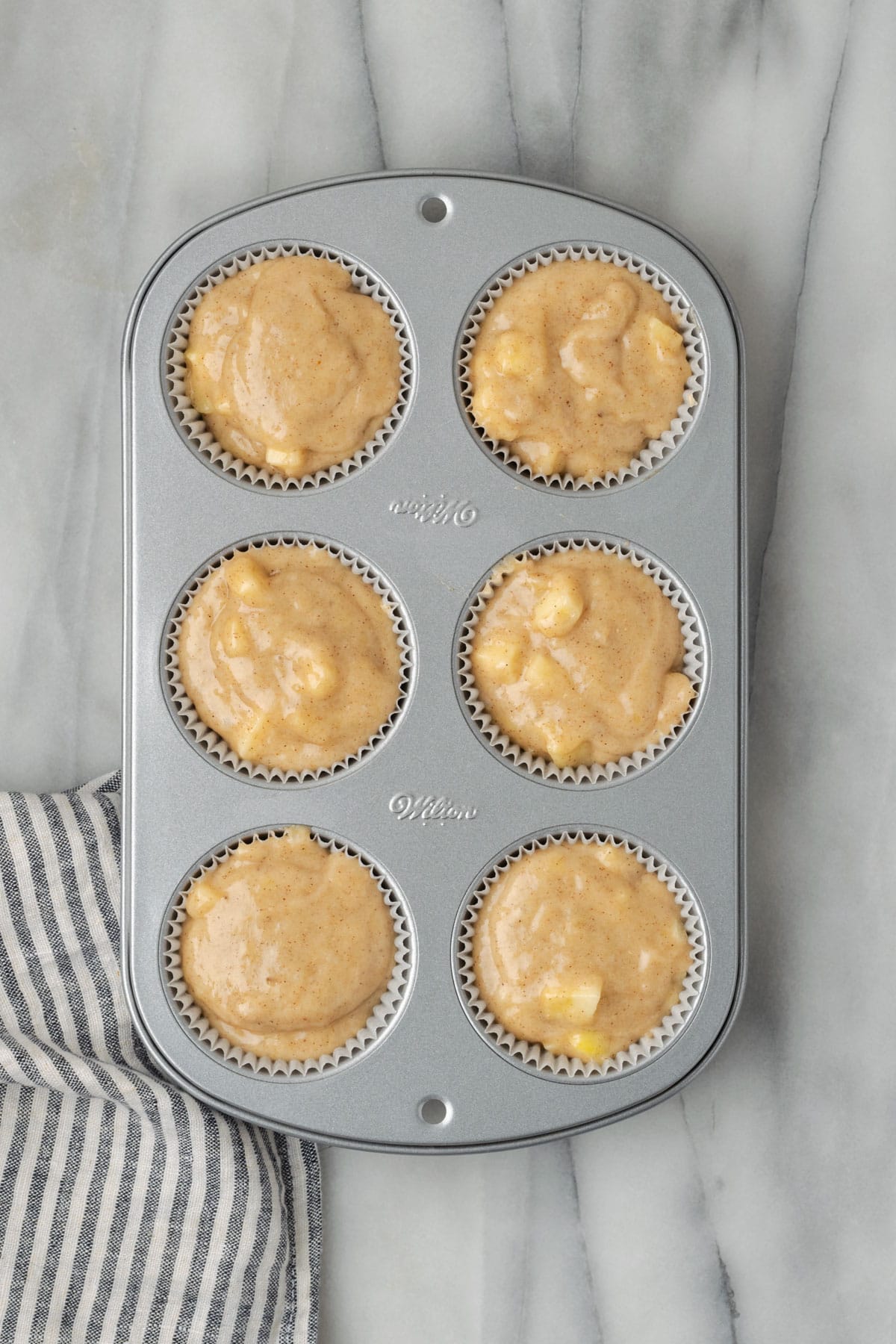 A six cup muffin tin filled with unbaked apple banana muffin batter.