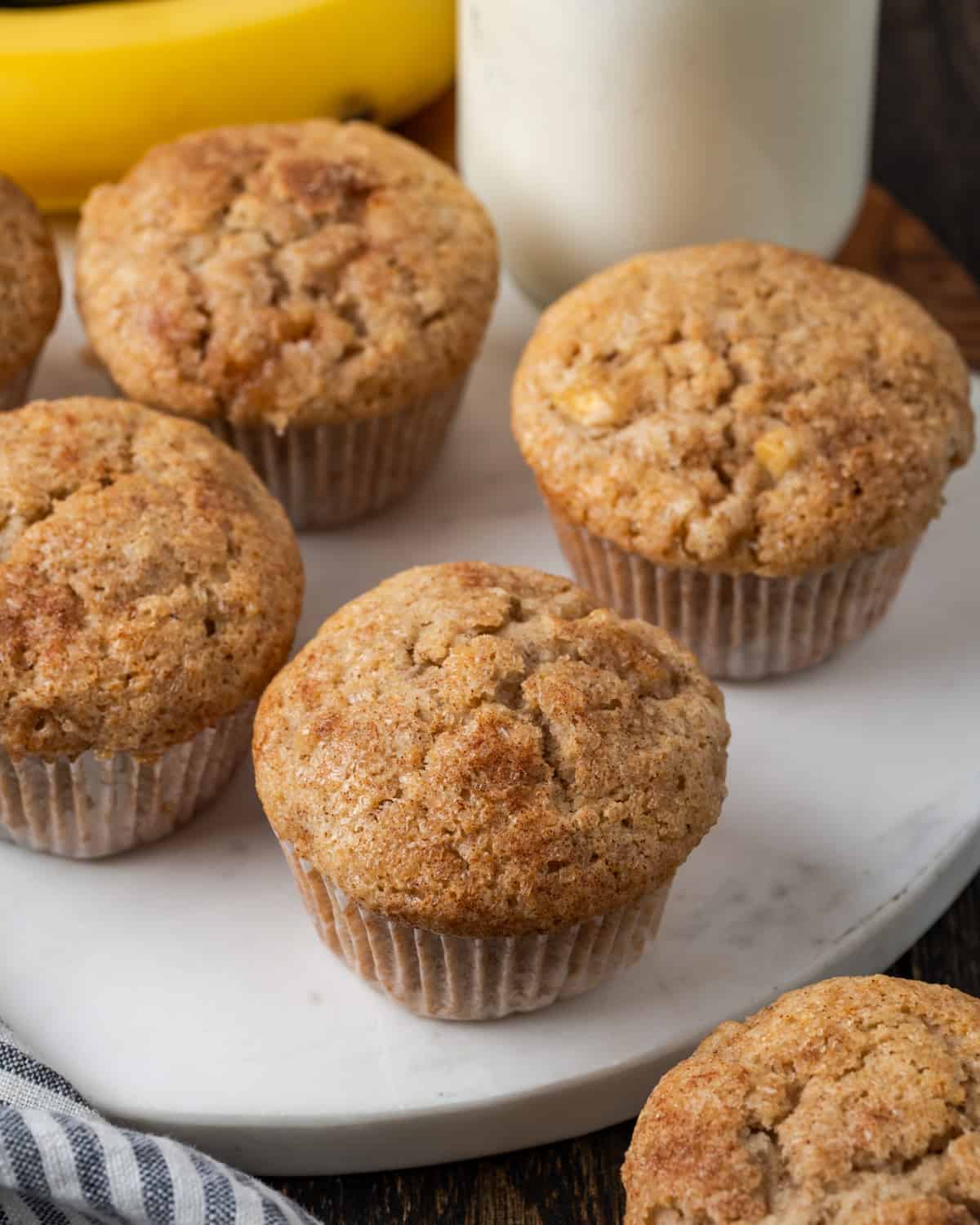 A batch of apple banana muffins sitting on a white marble cutting board.