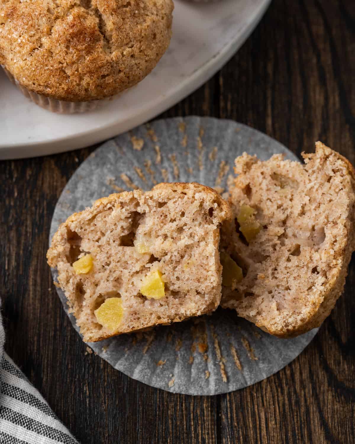 Two halves of a muffin on a table showing chunks of apples inside. 