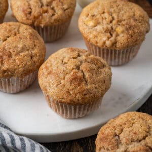 A batch of apple banana muffins sitting on a white marble cutting board.