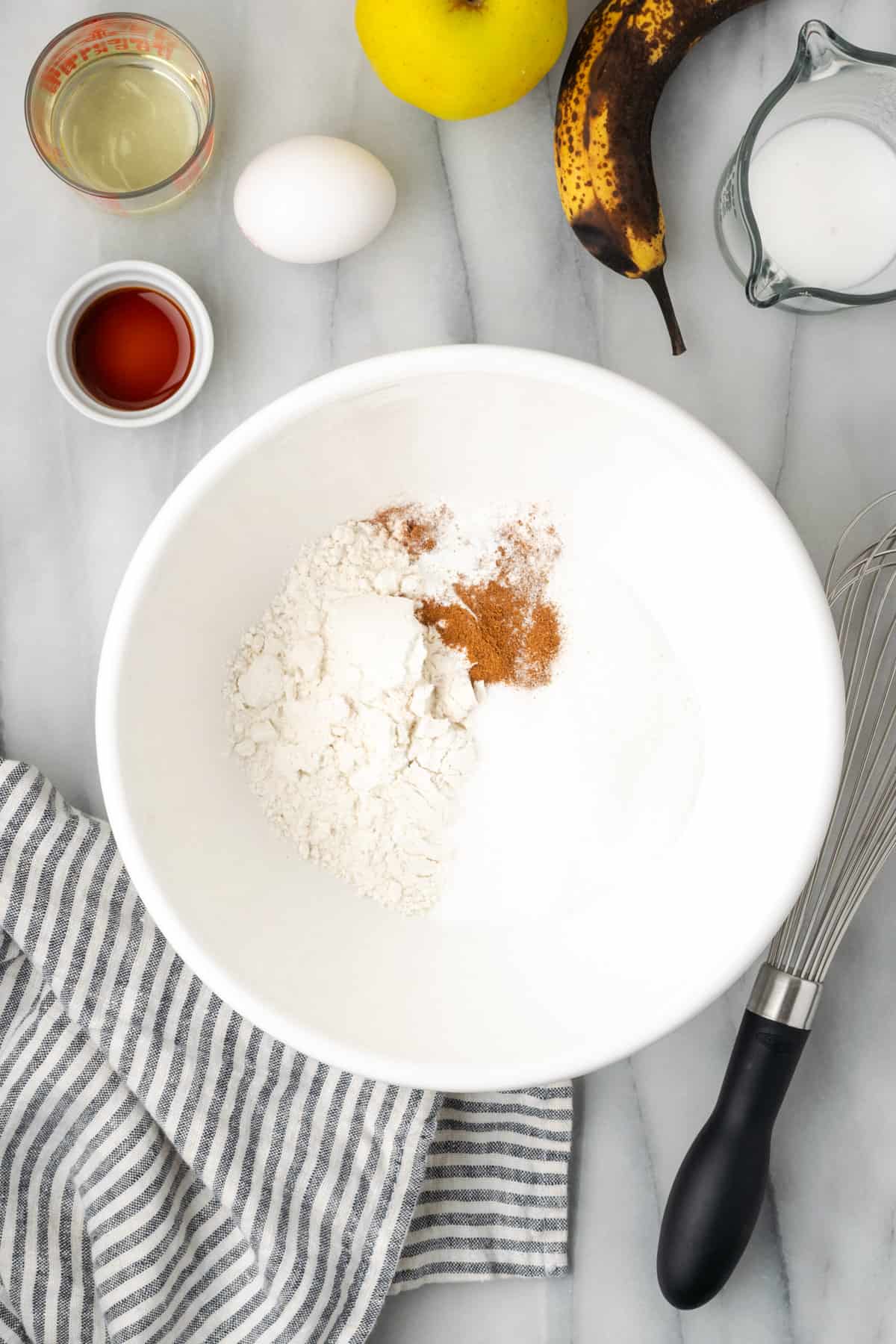 Gluten free flour, sugar, baking powder, salt and apple pie spice combined in a large white bowl.