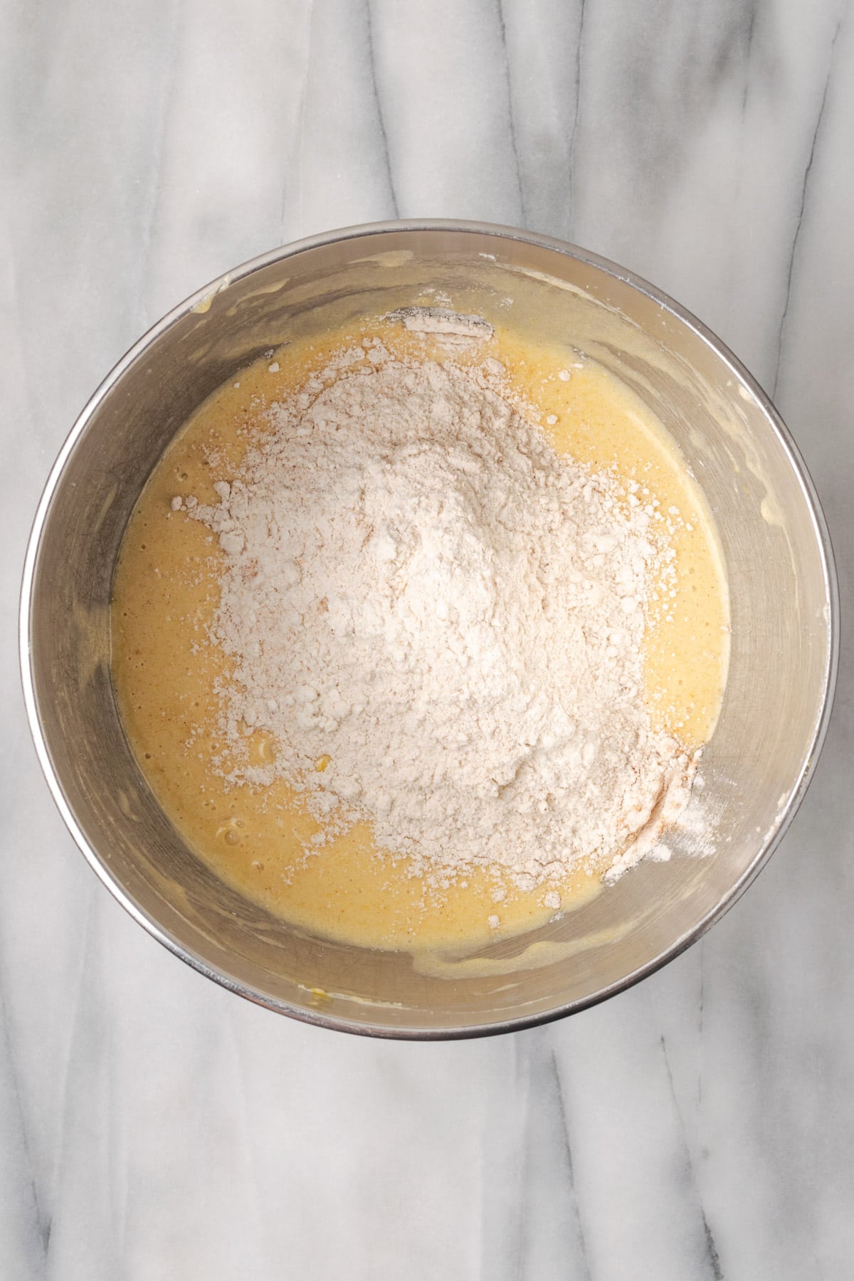 Dry ingredients being added to the mixing bowl with the partially mixed cake batter.