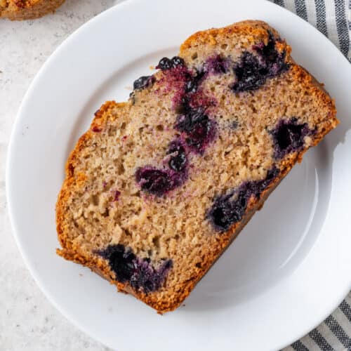 A slice of blueberry banana bread on white plate.