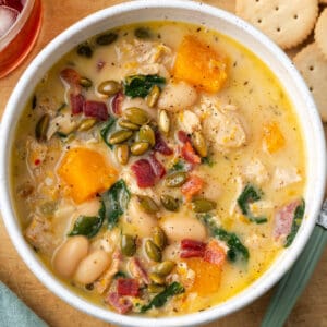 A bowl of chicken butternut squash soup topped with roasted pepitas and bacon pieces.