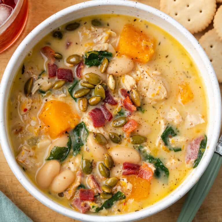 A bowl of chicken butternut squash soup topped with roasted pepitas and bacon pieces.