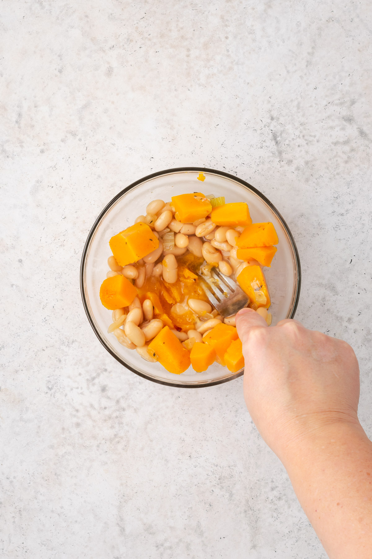 White beans and cooked squash being mashed in a small bowl.