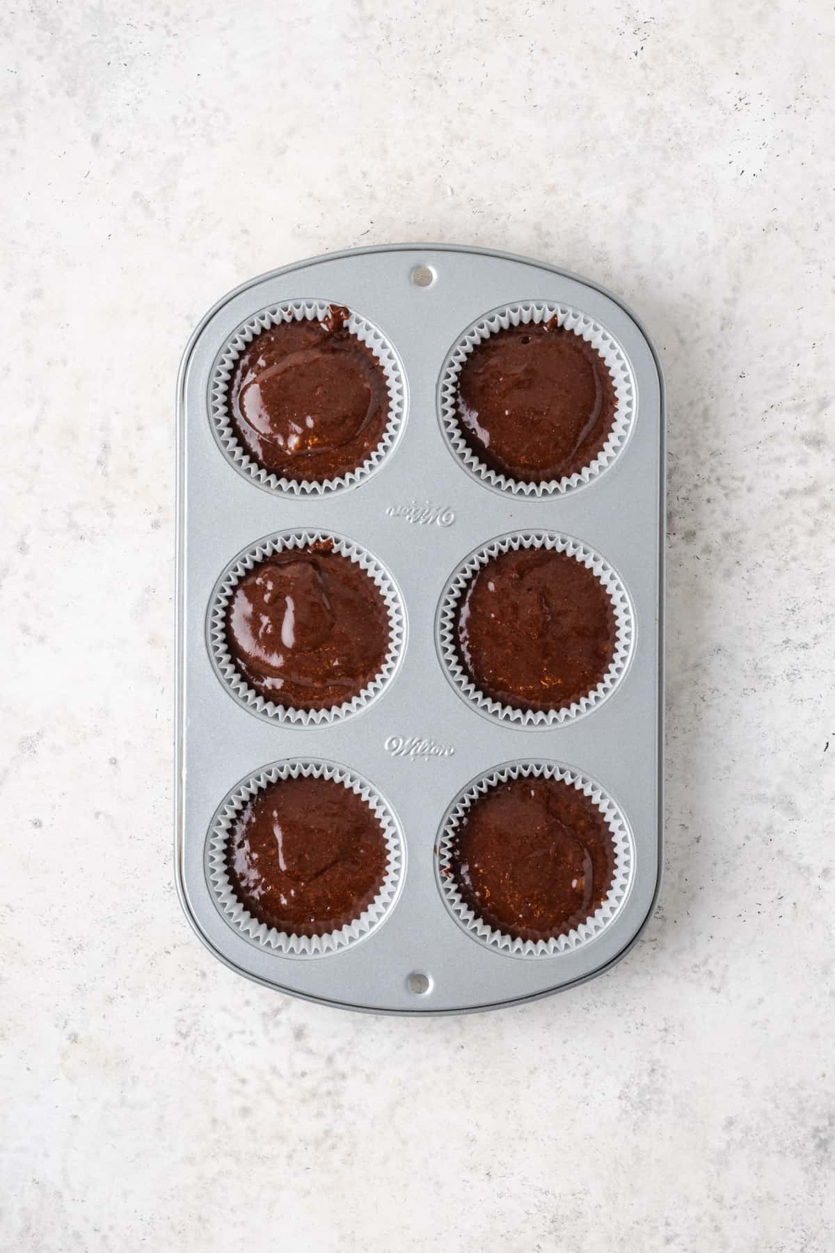 A 6-cup muffin pan filled with chocolate cupcake batter.