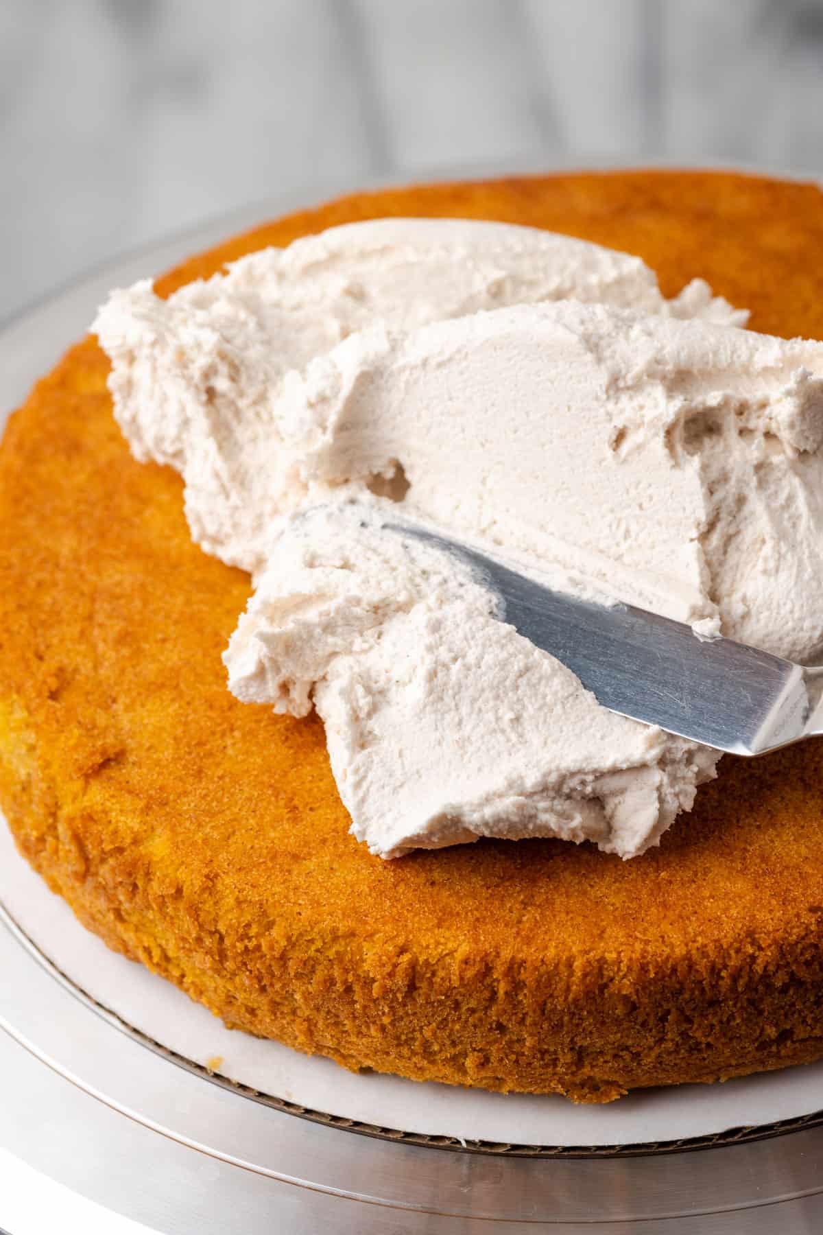 Cinnamon buttercream frosting being spread onto a layer on gluten free pumpkin cake with an offset spatula. 