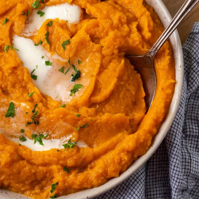 A bowl of mashed sweet potatoes topped with melted butter.