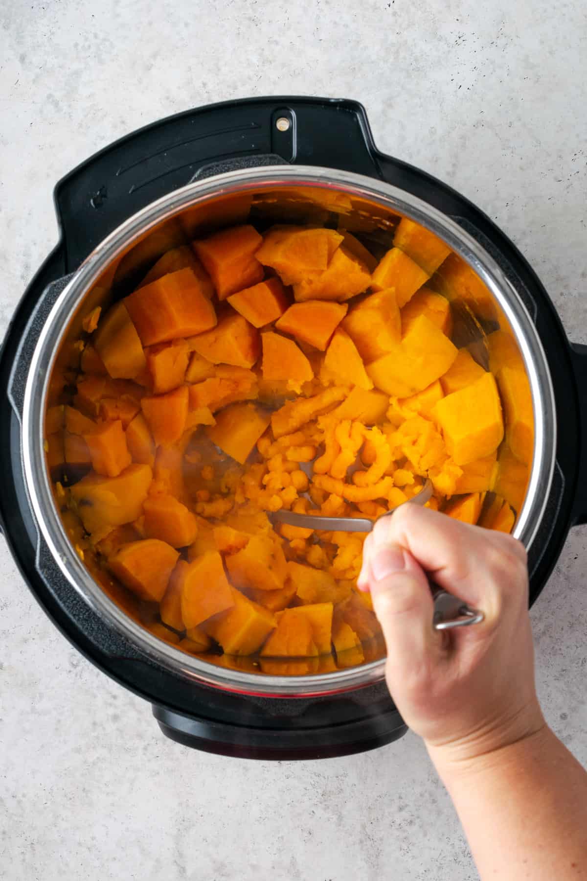 A potato masher being used to squish cooked sweet potatoes.