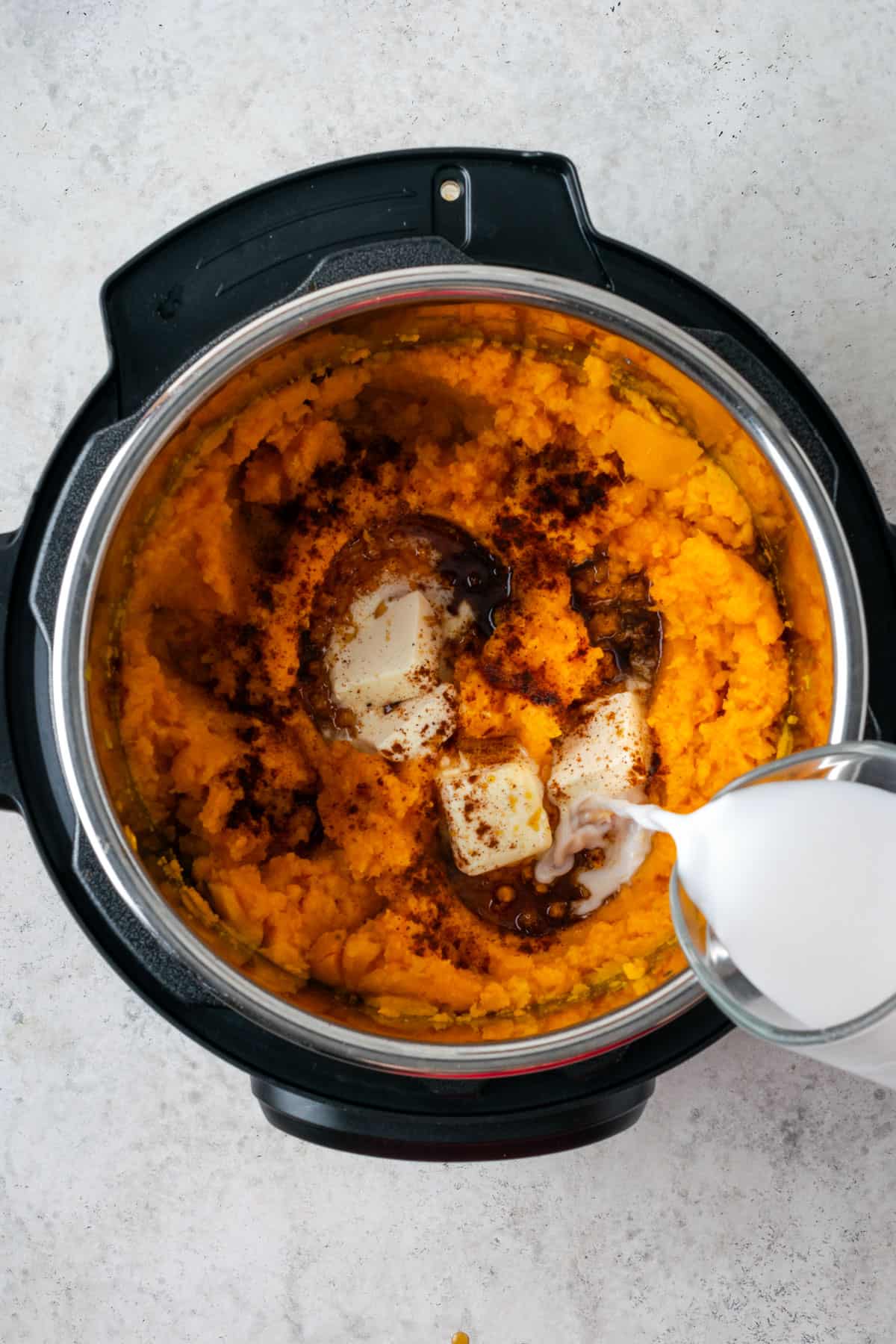 Chili powder, maple syrup, vegan butter and non-dairy milk being added to the sweet potato mash.