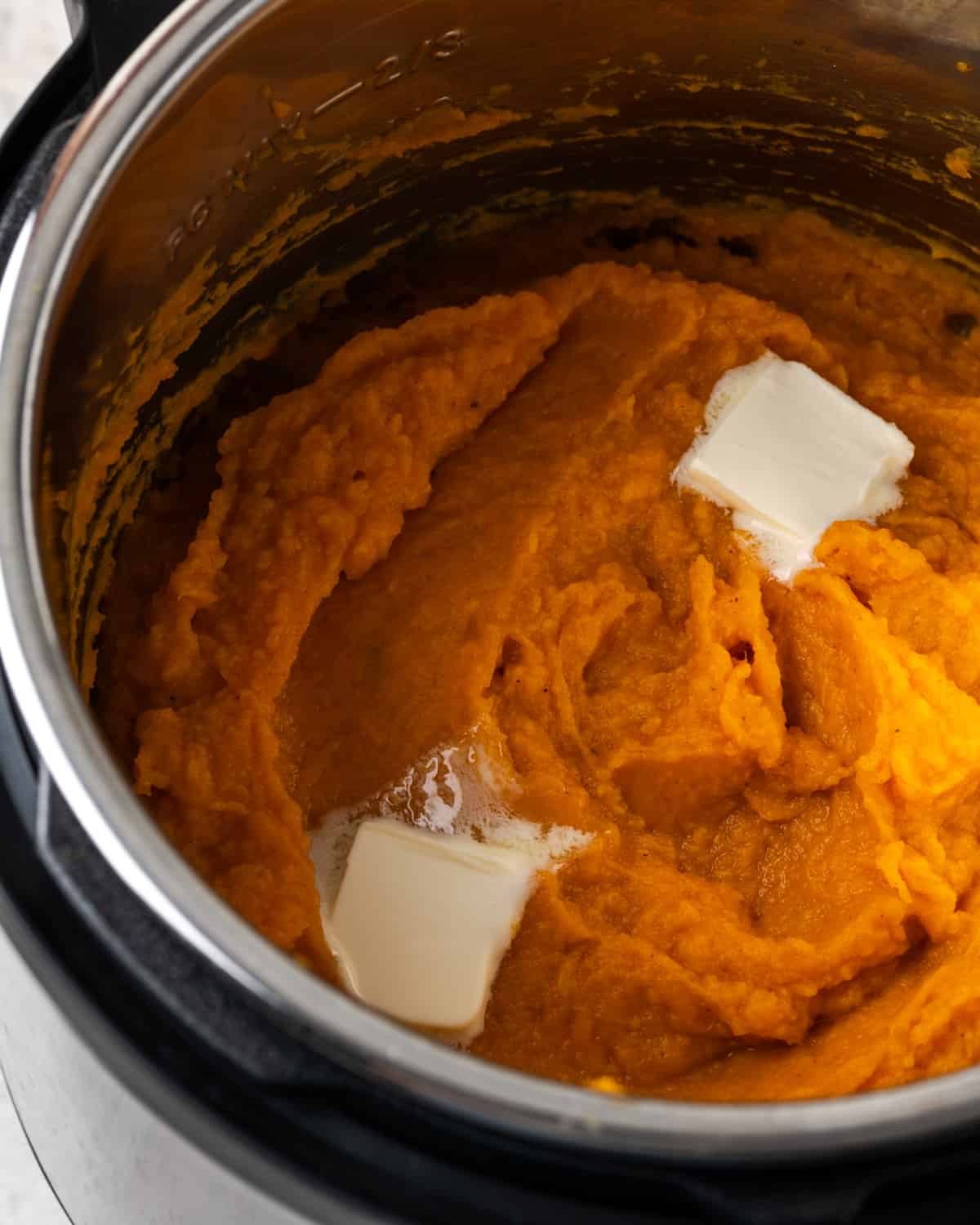 Mashed sweet potatoes topped with melting butter inside an Instant Pot.