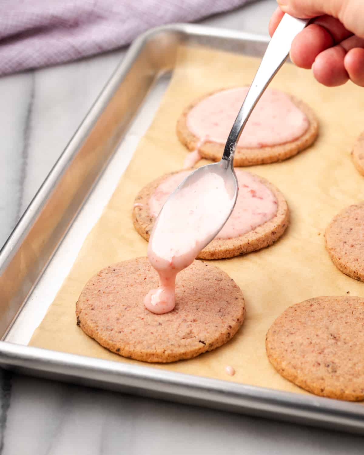 Pink icing pouring onto a strawberry shortbread cookie.