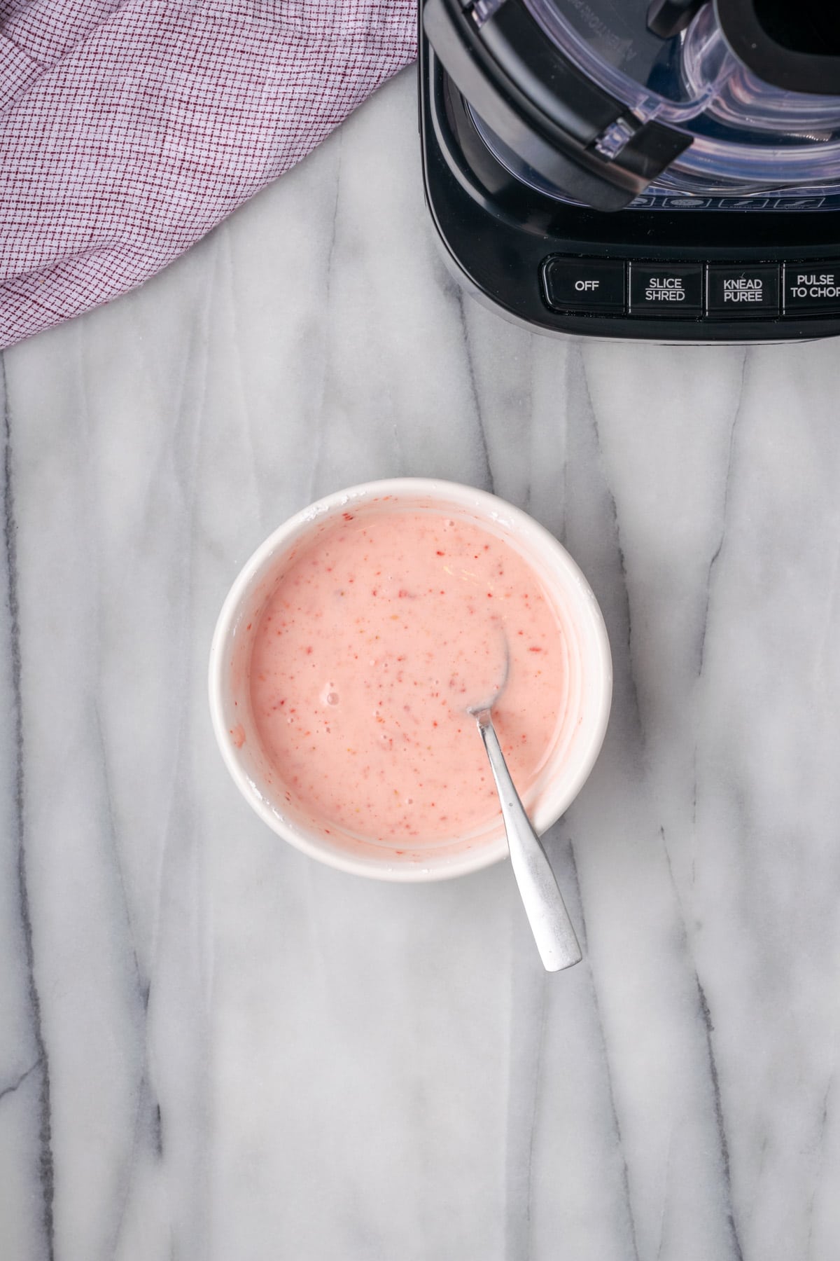 A bowl of pink icing with a spoon. 