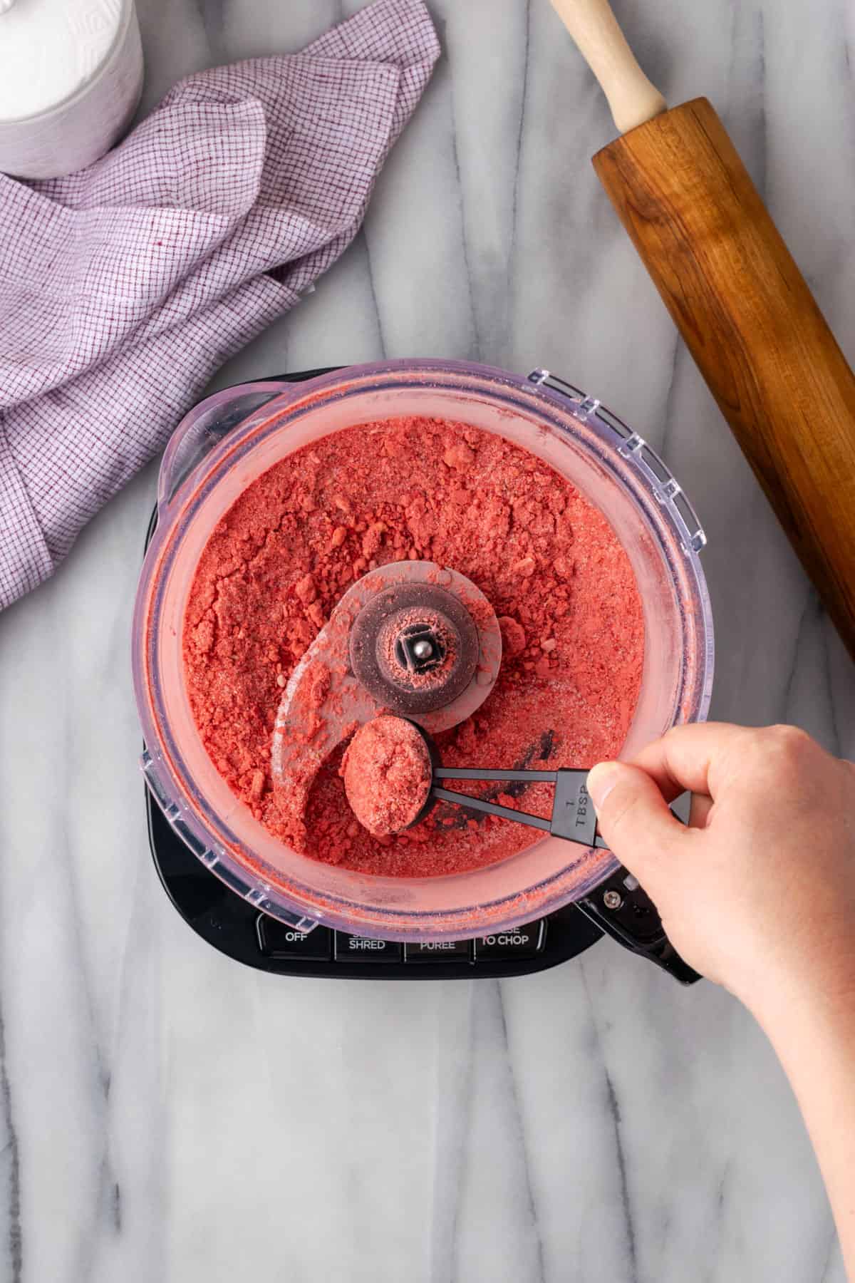 Strawberry powder being scooped from the food processor with a measuring spoon.