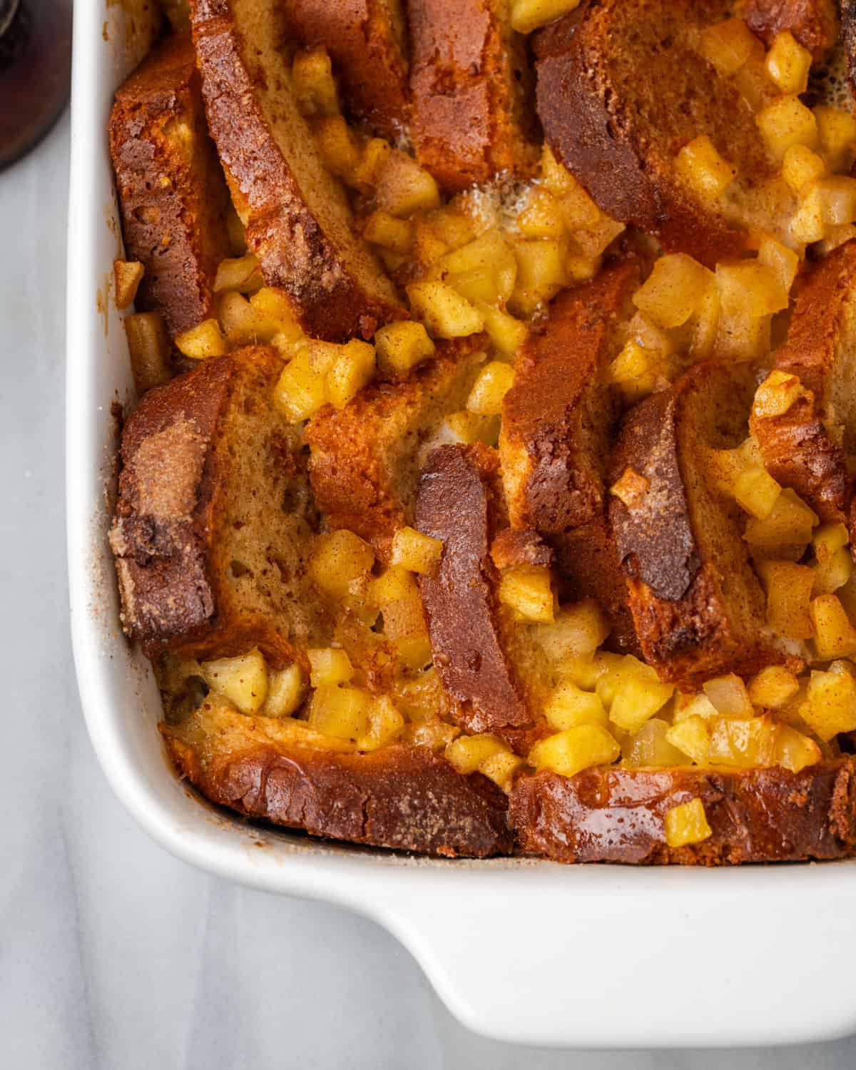 A baking dish of brioche baked french toast topped with apple pieces and brown sugar cinnamon. 