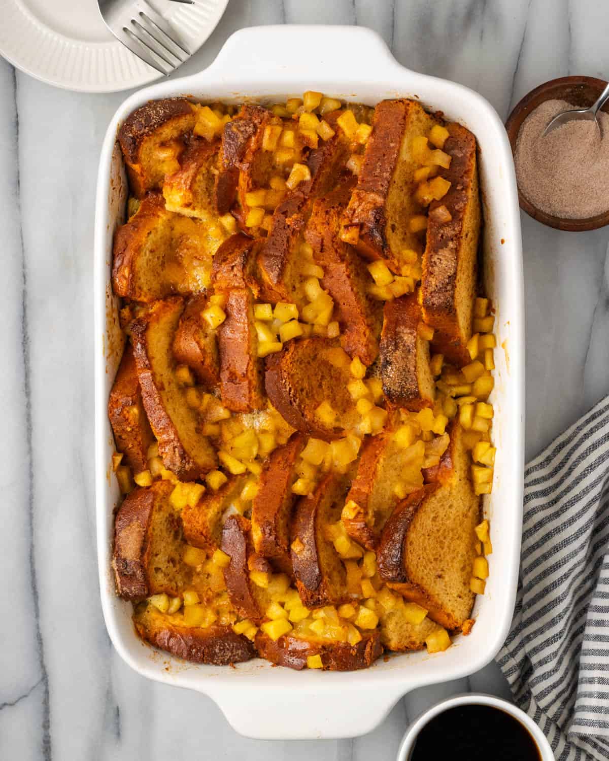 A pan of freshly baked gluten free brioche french toast topped with apples sitting on a white table.