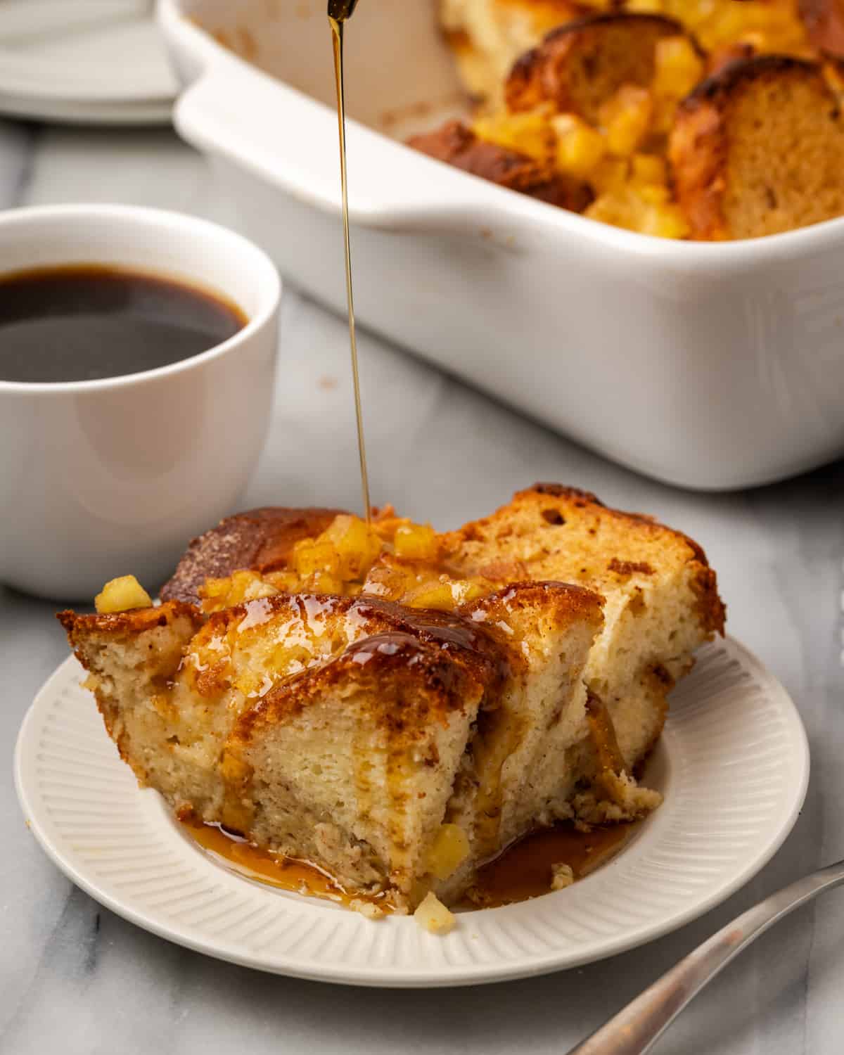 A square of brioche baked french toast served on a white plate and topped with syrup. 