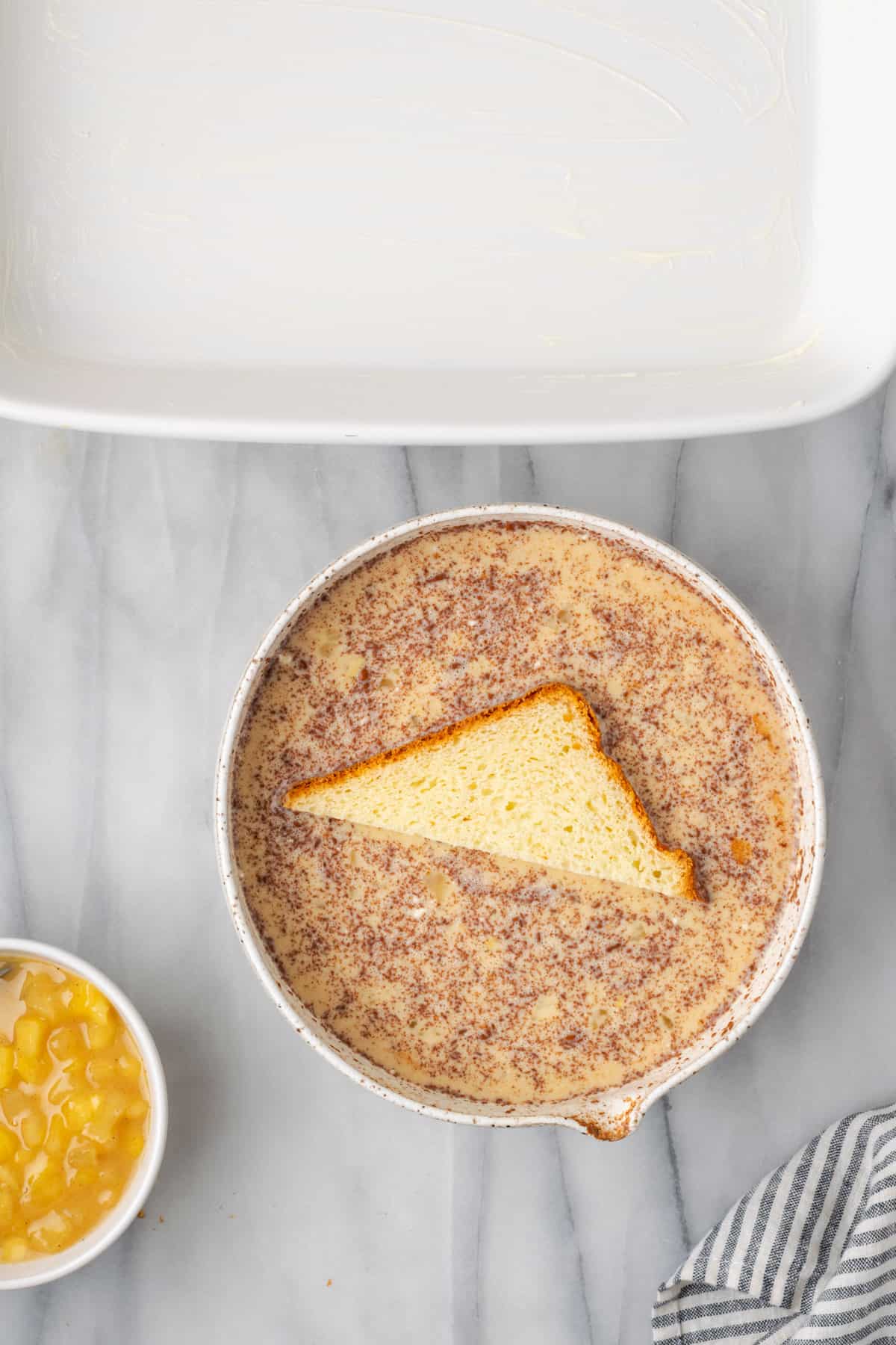 A slice of bread being dipped into the egg mixture.