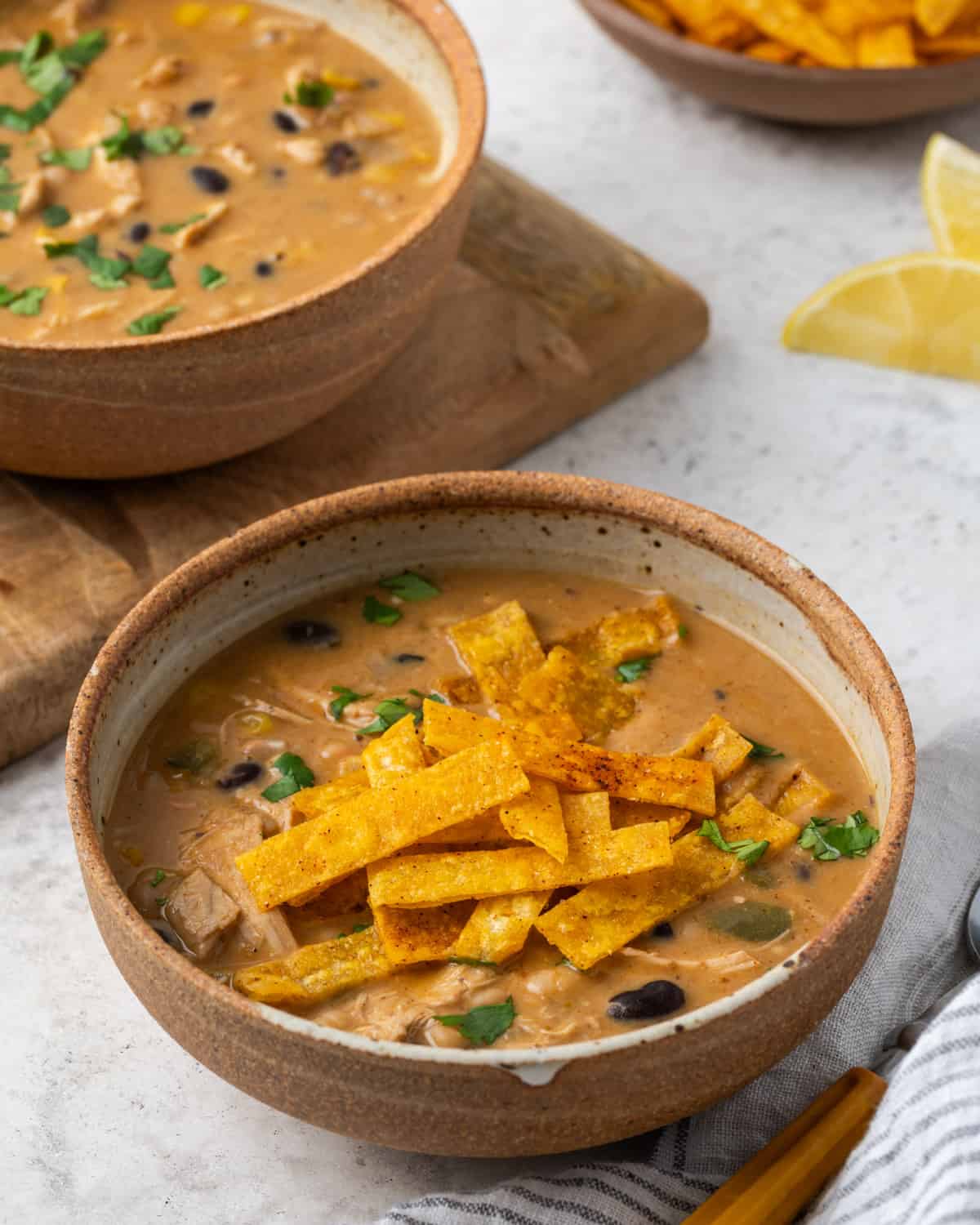 Two bowls of chicken tortilla soup being served on a white table.