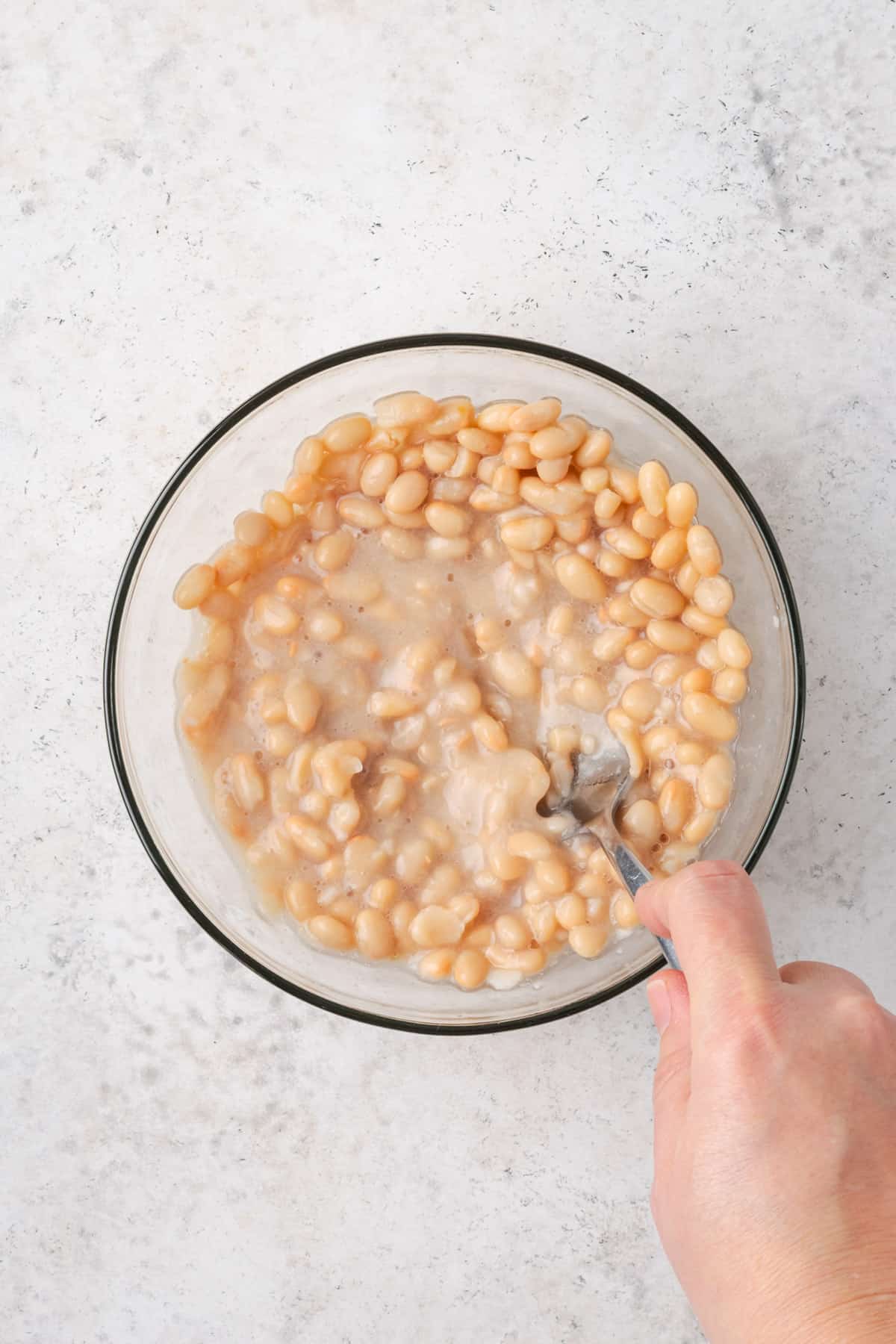 A can of navy beans being mashed with a fork in a small bowl.