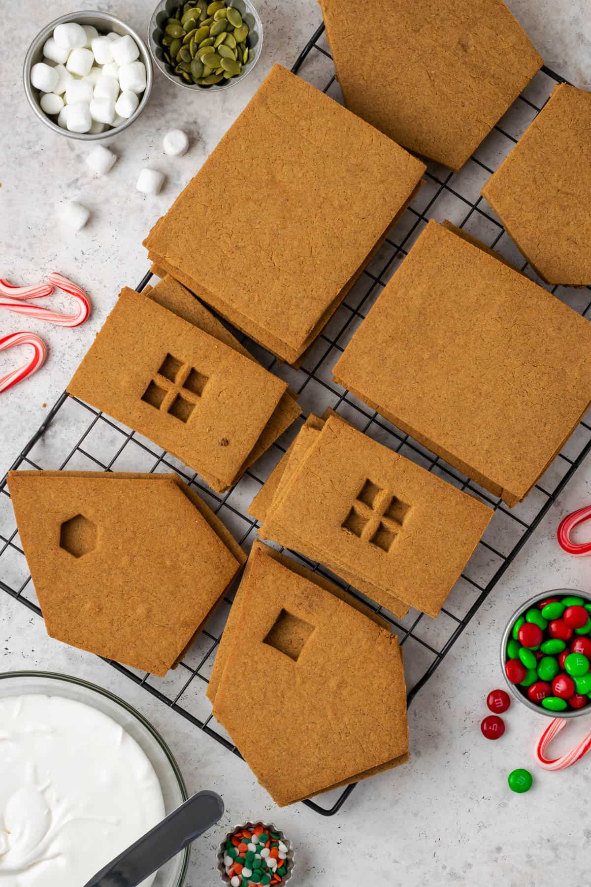 Gluten-free gingerbread house pieces sitting on a cooling rack surrounded by dishes of candy. 