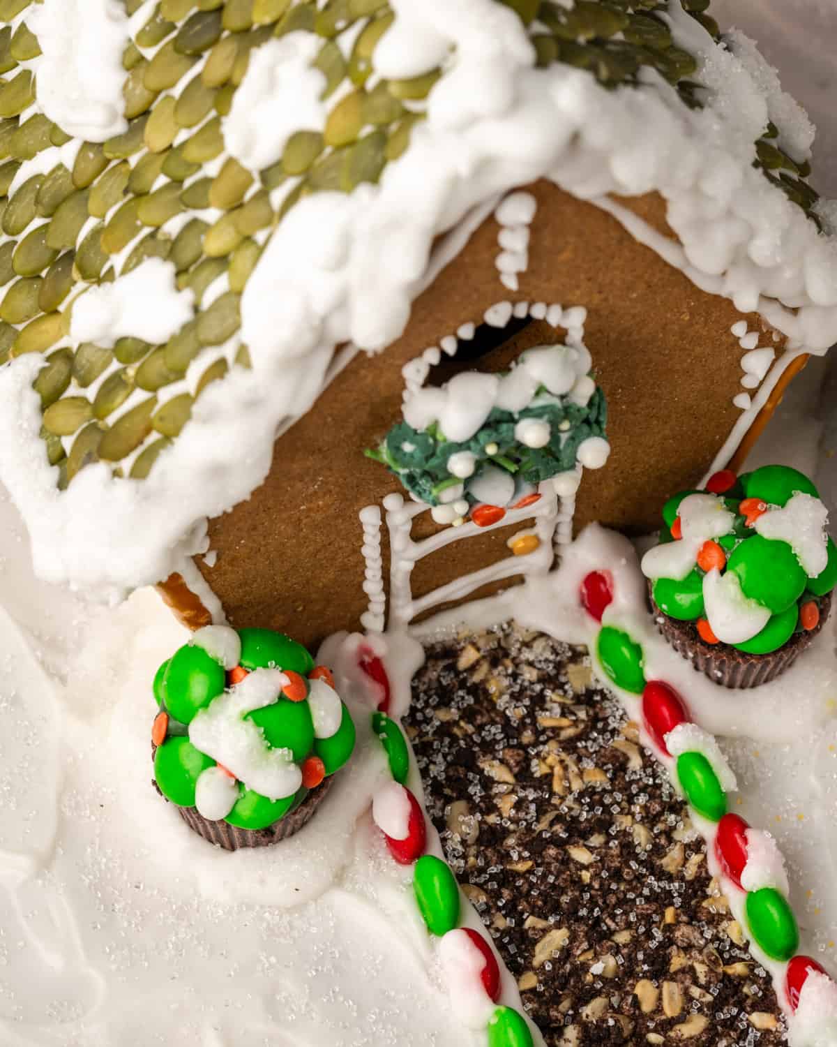 A gluten free gingerbread house covered with snow icing, showing bushes and a path made from candy.