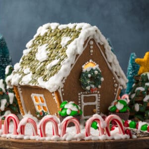 A gluten free gingerbread house surround by candy decorations and a candy cane fence.