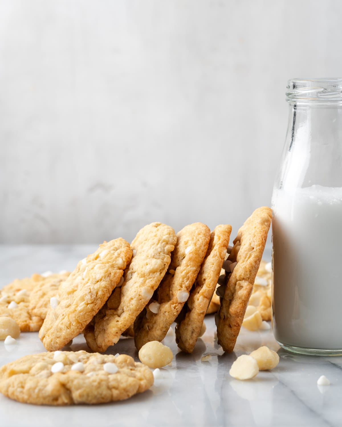 A stack of gluten free white chocolate macadamia nut cookies leaning against a jar of milk.