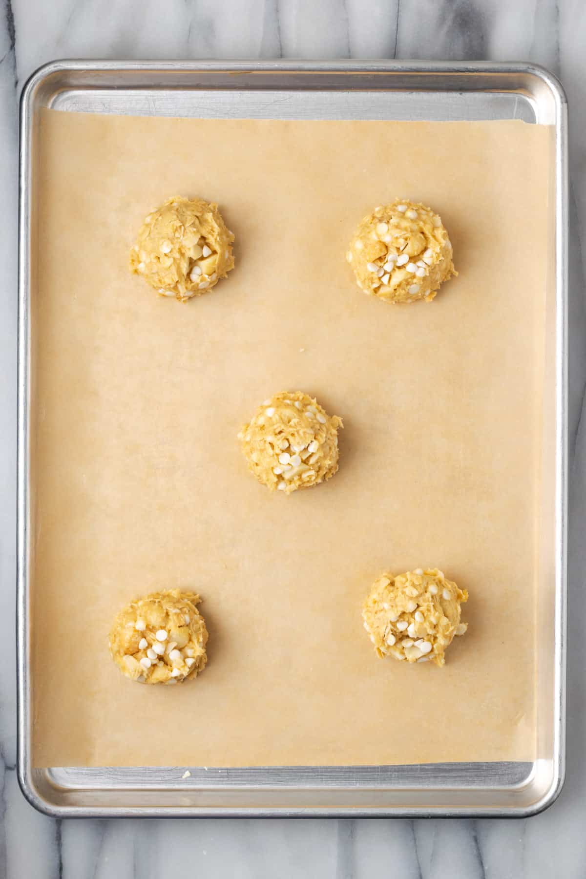 Balls of white chocolate macadamia nut cookie dough on a baking sheet.